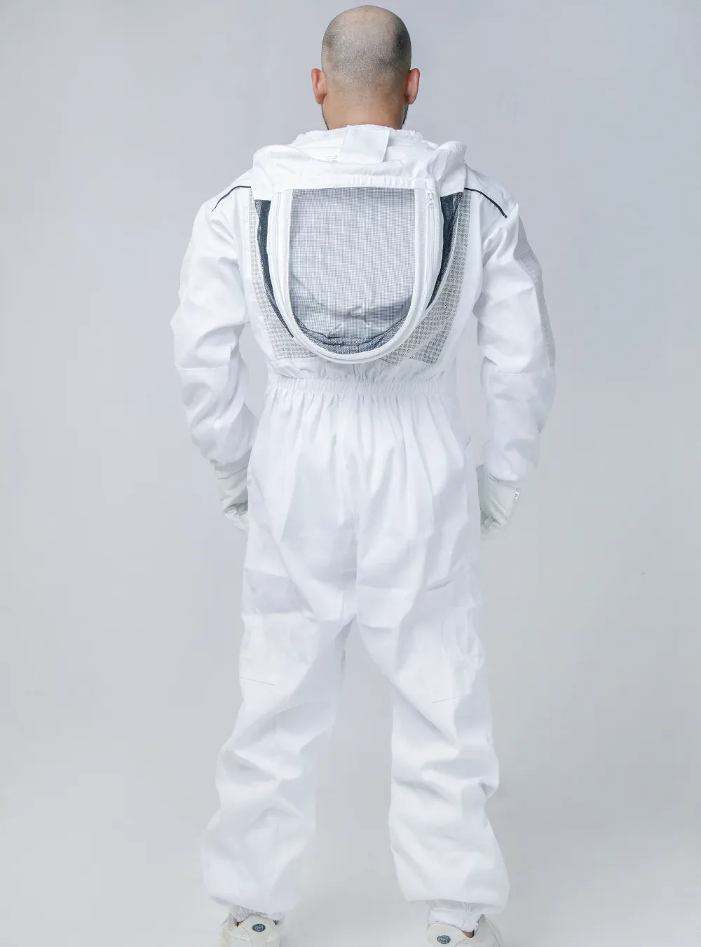 Back view of a beekeeper in a white semi-vented suit with the fencing veil folded back, showing the shoulder seams and back panel
