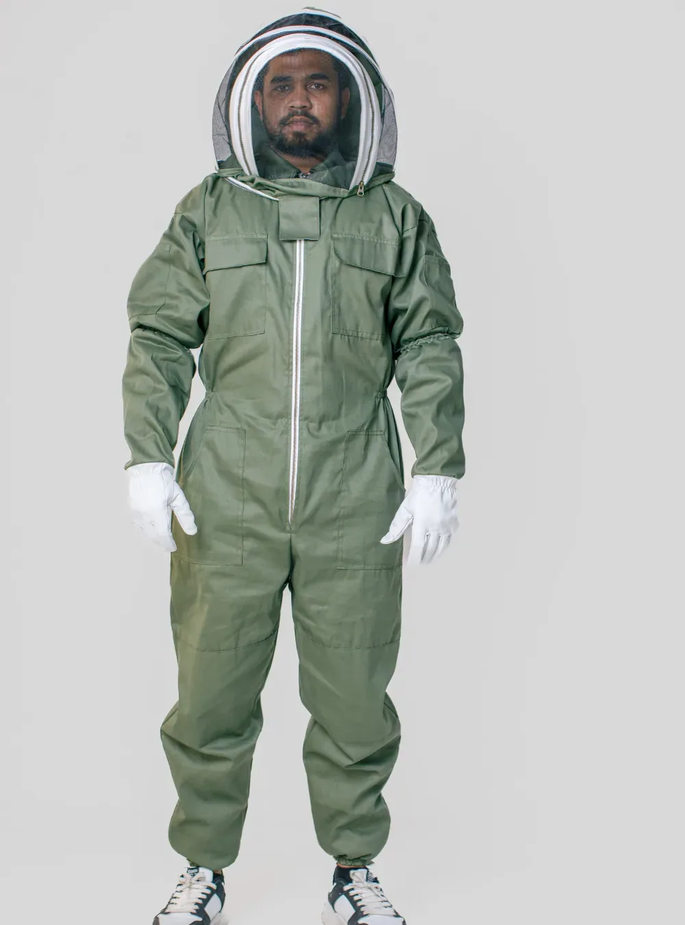 Front view of a beekeeper in an olive cotton suit with a fencing veil, with the suit legs worn over trainers